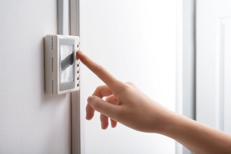 woman's hand turning up a thermostat to save energy