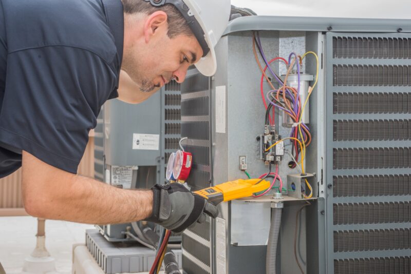 An HVAC technician works on an outdoor AC unit