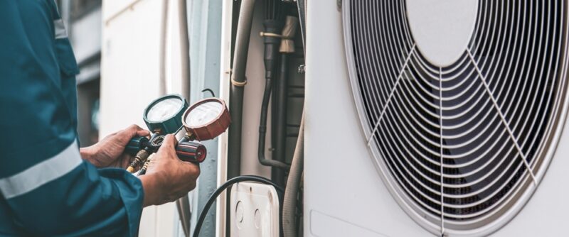 Heat and Air Conditioning, HVAC system service technician using measuring manifold gauge checking refrigerant and filling industrial air conditioner after duct cleaning maintenance outdoor compressor.